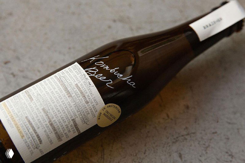 Крупный план лежащей бутылки Brain+er: подробная текстовая этикетка, белые рукописные зарисовки и лёгкий леттеринг на поверхности стекла в декоративном стиле.