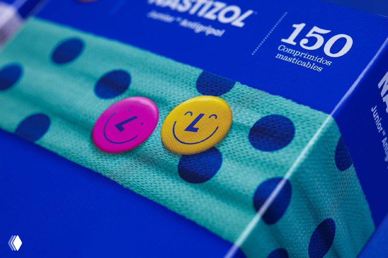 Крупный план упаковки Nastizol с текстурой шарфа и двумя смайликами-значками на коробке на фирменном синем фоне.