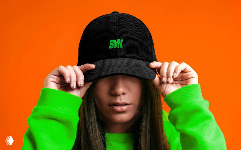Модель в чёрной кепке и ярко‑зёленой толстовке с вышитым знаком BVN — мерч и брендовые элементы айдентики, подчёркнутые контрастной палитрой и графикой.