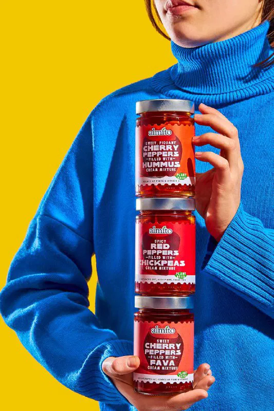 Человек в синем свитере держит три банки Almito одна на другой на жёлтом фоне; подчёркнута компоновка и цветовая контрастность.