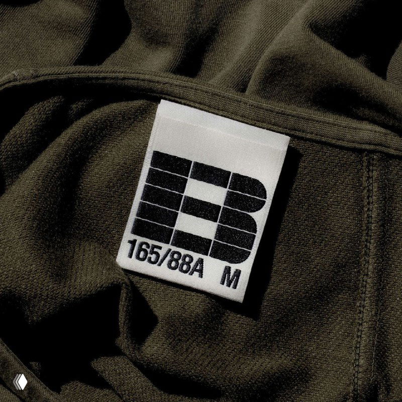 Этикетка на одежде с модульной литерой «B» и размерной маркировкой; пример применения айдентики на текстильной бирке.