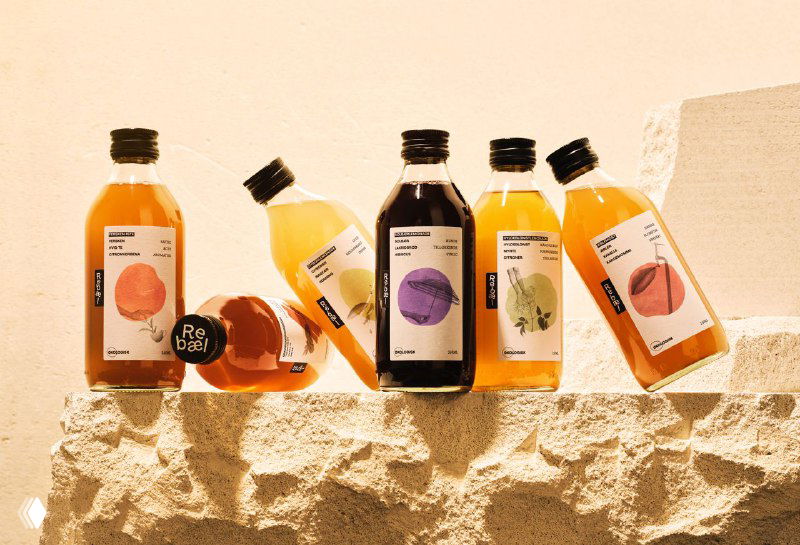 Несколько бутылок Rebæl разных вкусов на рваной каменной поверхности — показ серии упаковок с акцентом на цвет и этикетку.