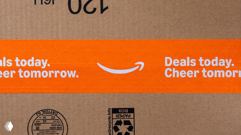 Крупный план упаковочной ленты с оранжевыми элементами и стрелкой‑логотипом Amazon — акцент на деталях печати и материалов после редизайна.