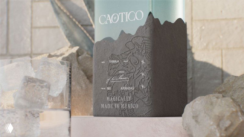 Крупный план рельефной этикетки Caotico с горным силуэтом и тиснением, бутылка на фоне камней, видна текстура бумаги и рельеф.