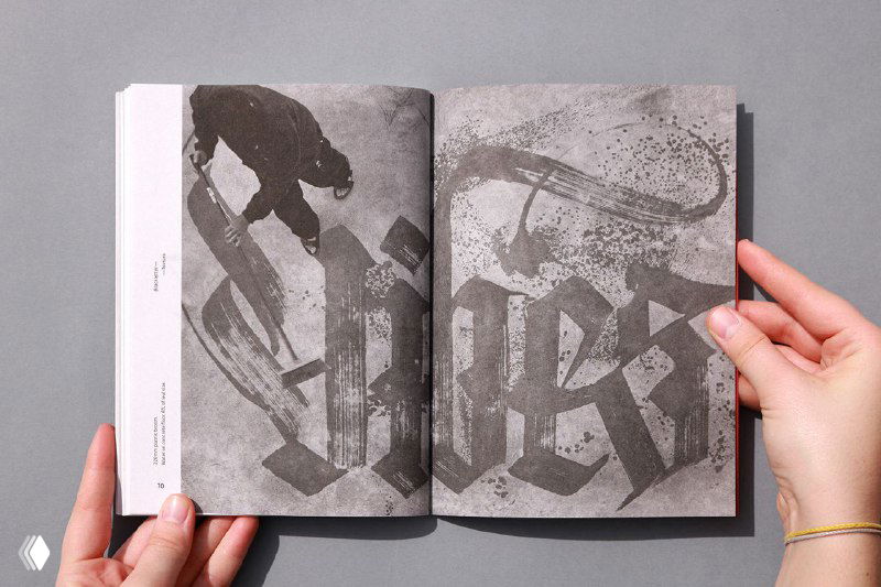 Двухстраничный разворот зина «Blackletter. Textura» с монохромными иллюстрациями и каллиграфическими композициями; вид в руках у человека.