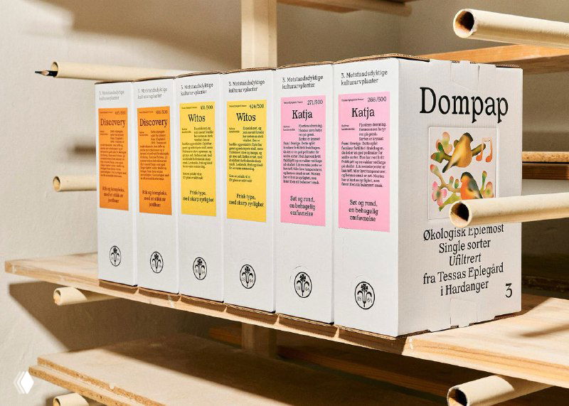 Ряд коробок Tessas Eplegard в линию; спереди видна однообразная монохромная типографика и цветные полосы-этикетки, указывающие вкусы и сорта.