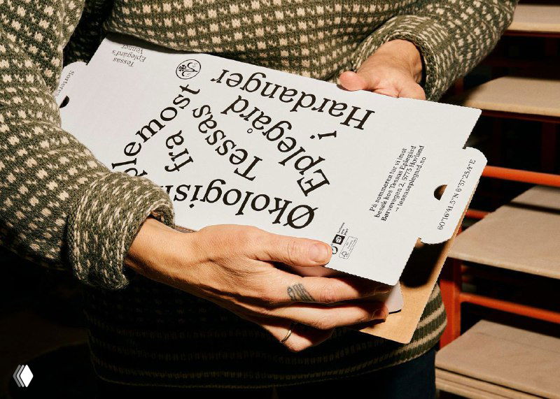 Крупный план рук, распаковывающих коробку Tessas Eplegard; хорошо видно внутреннюю конструкцию и печать с крупными словами на коробке.