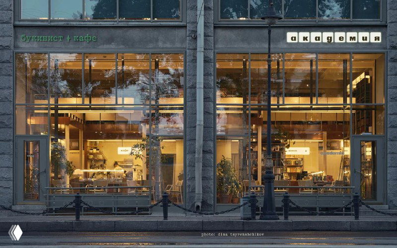Фасад магазина‑кафе «Академия» с большими стеклянными витринами и тёплым освещением, видно оформление входной группы и элементы фирменной айдентики.