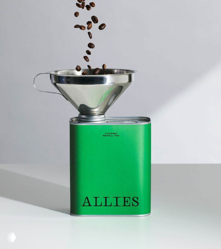 Кофейные зёрна падают в металлическую воронку над зелёным кофемолом Allies — студийная фотография продукта и процесса.