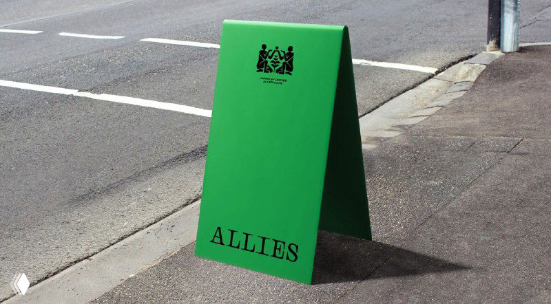 Зелёный уличный штендер с крупным логотипом Allies на тротуаре — пример наружной рекламы в фирменном цвете.