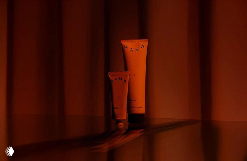 Тубы косметической упаковки Mana на глянцевой поверхности в насыщенном оранжево-красном световом решении, акцентирующем плавные градиенты дизайна.