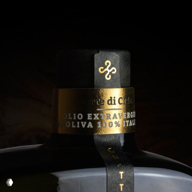 Крупный план горлышка бутылки с чёрной пробкой и золотой фольгой; читается надпись «OLIO EXTRAVERGINE OLIVA 100% ITALY».