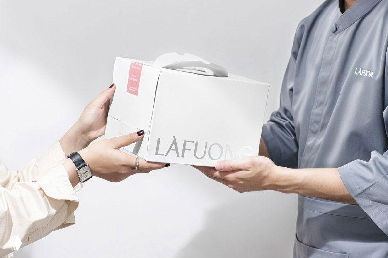 Передача коробки LaFuong из рук в руки в светлом кадре; видно логотип на торце и чистую, премиальную эстетику упаковки.