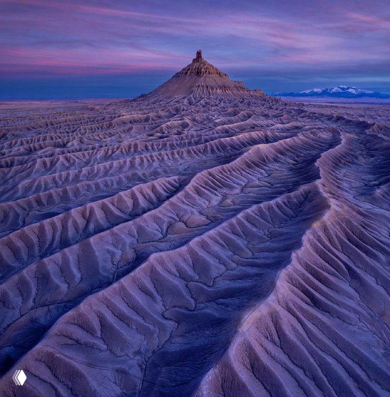 Эрозионные формы пустынного плато в фиолетово-сиреневых тонах на рассвете: аэрофотография подчёркивает рельеф и текстуру поверхностей.
