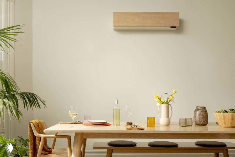 Интерьерная сцена с обеденным столом, растением и настенным блоком кондиционера — визуализация применения климатической системы Quilt в домашнем окружении.