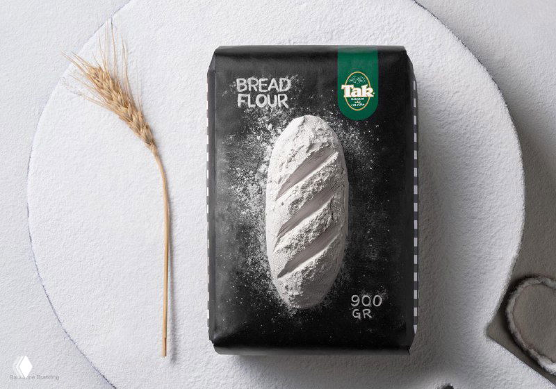 Пакет 'Bread Flour' от Tak на круглой белой подложке рядом с колоском пшеницы; крупный план упаковки и фактуры муки, проект Backbone Branding.