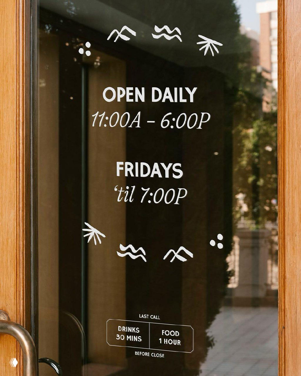 Наклейка на стеклянной двери с графикой и часами работы «OPEN DAILY 11:00A – 6:00P» и мелкими фирменными пиктограммами — применение айдентики в интерьере.
