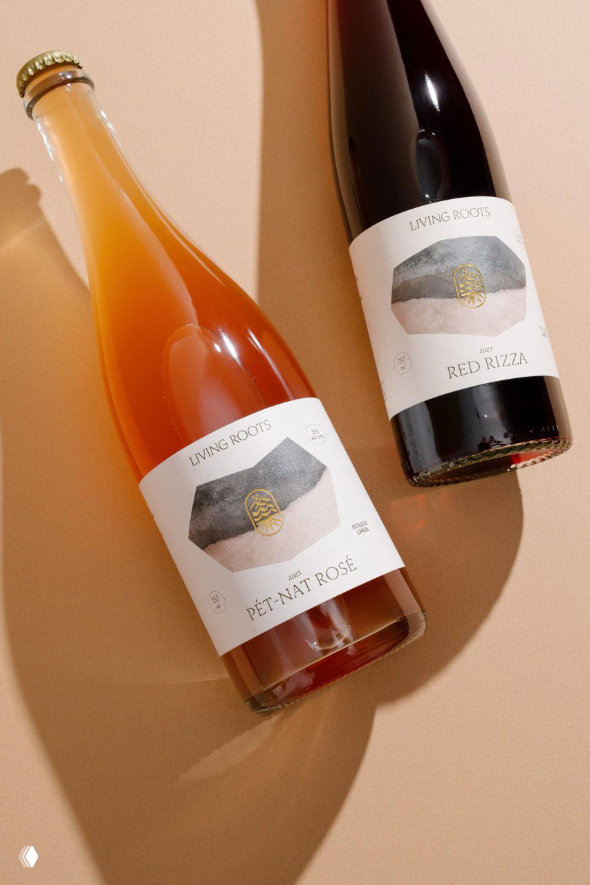Две бутылки Living Roots на светлом фоне: Pét-Nat Rosé и Red Rizza с минималистичной белой этикеткой и золотым логотипом — фотостиль упаковки.
