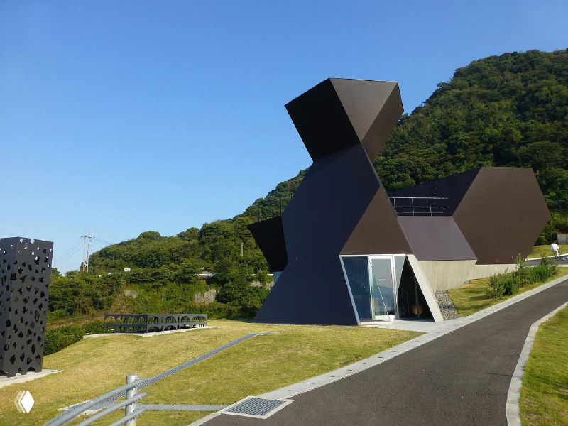 Нестандартный модульный тёмный павильон на зелёном склоне, асимметричные геометрические формы в ландшафте — экспериментальная архитектура музея.