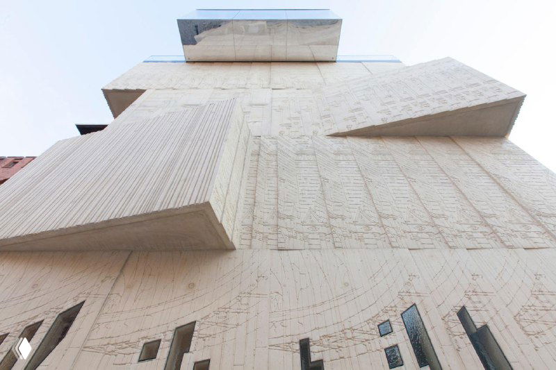 Монументальная текстурированная стена с выступающими прямоугольными объёмами и резным орнаментом — фасад крупного здания-музея с рельефной отделкой.