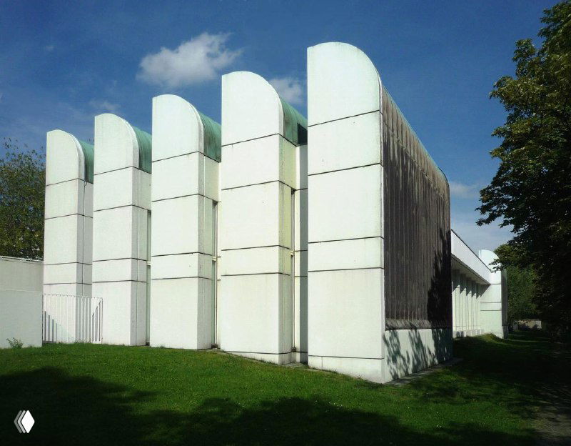 Белое здание с серией аркообразных вертикальных объёмов, подчеркнутых тенью; пример модернистских приёмов в проектировании музейных пространств.