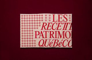 Плоский ракурс обложки книги на бордовом фоне с крупным шрифтом «LES RECETTES PATRIMOINE QUÉBECOIS» и графическим узором.