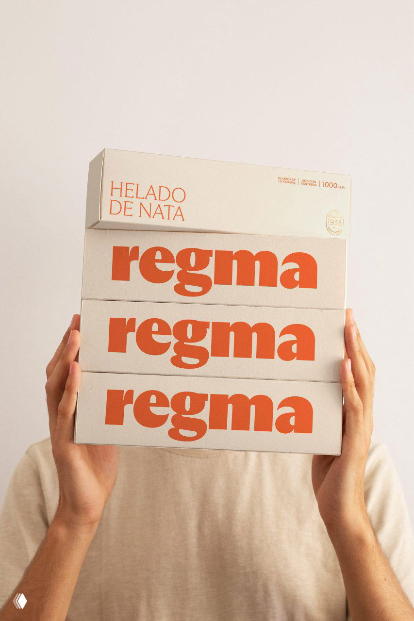 Человек держит стопку коробок Regma с оранжевым логотипом на светлом фоне, акцент на масштабе и визуальной простоте упаковки бренда.