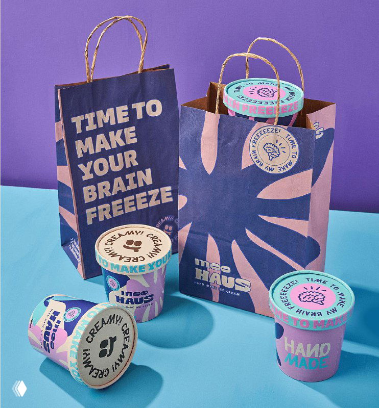 Композиция с бумажными пакетами и баночками Moohaus на столе, яркий фиолетово-голубой фон и акцент на фирменной упаковке и этикетках.