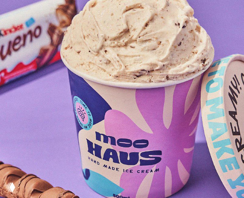 Баночка Moohaus с аккуратно выкладыванным шаром мороженого на фиолетовом фоне; демонстрация текстуры продукта и дизайна упаковки.