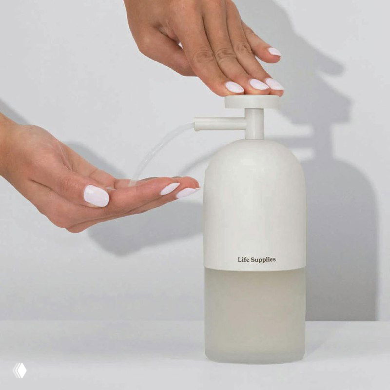 Крупный план диспенсера Life Supplies: белая минималистичная помпа и прозрачный флакон на однотонном фоне, подчёркнута эргономика и простота.