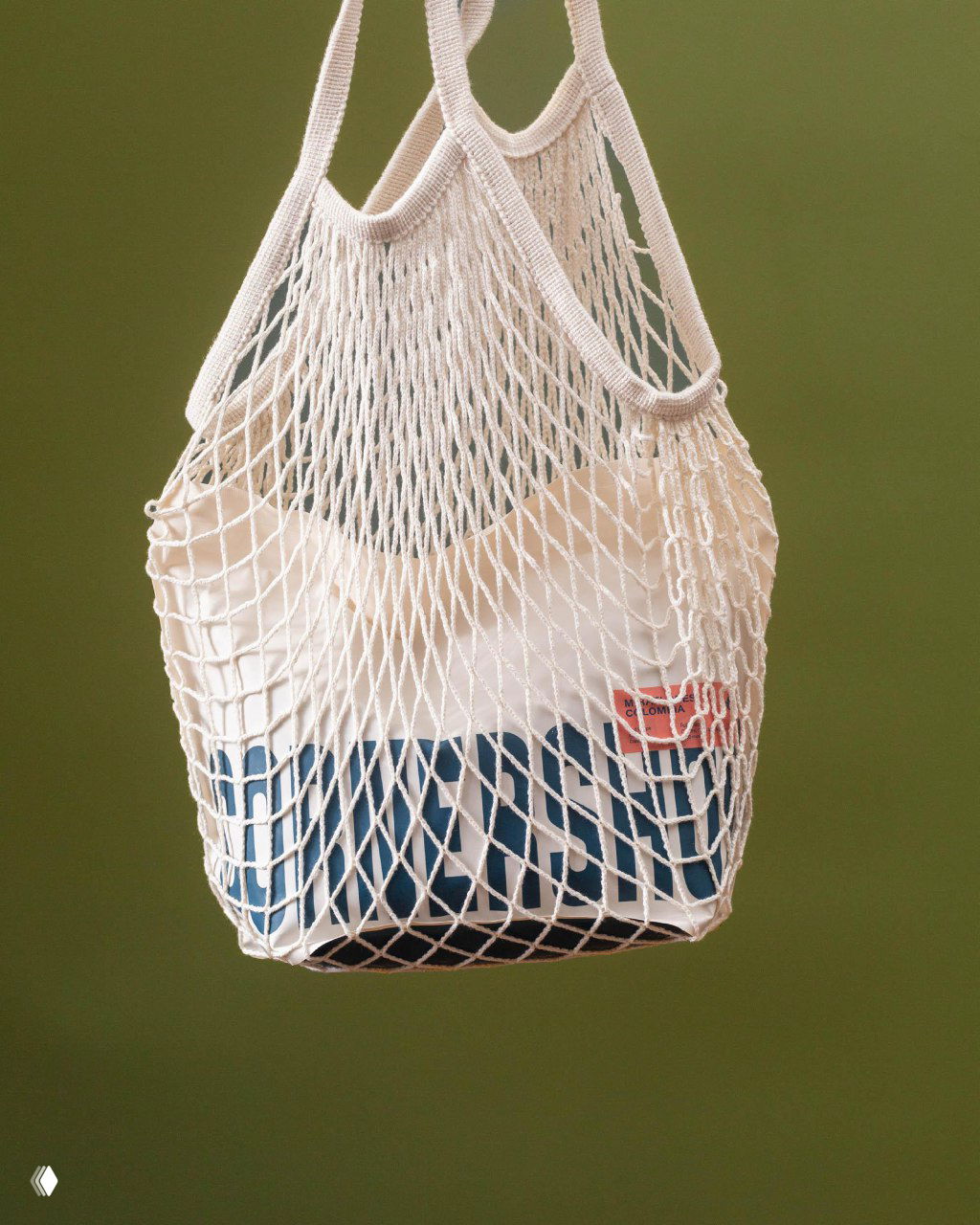 Сетчатая эко-сумка с пакетом CORNERSHOP внутри на зелёном фоне; фотография подчёркивает мерч, логотив и эстетическую привязку к устойчивости.