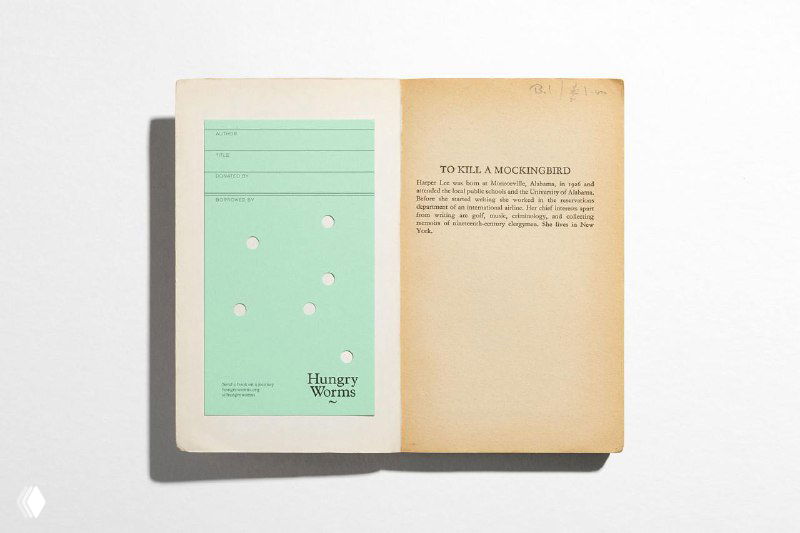 Открытая старая книга с вставленной фирменной вкладкой/закладкой Hungry Worms — сочетание физической коллекции и нового визуального языка проекта.