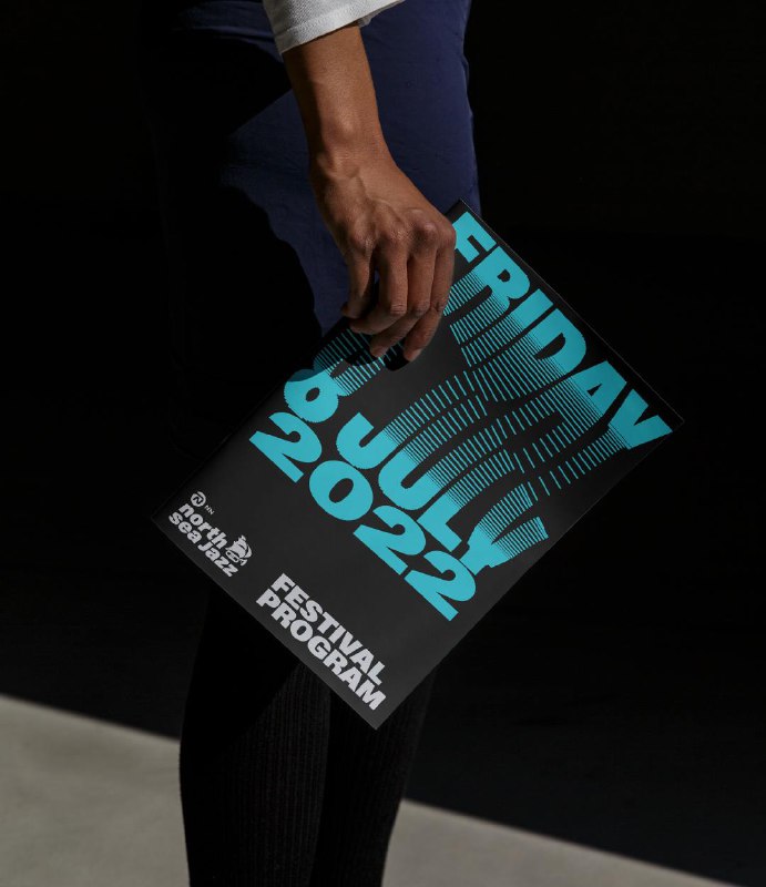 Рука держит программку фестиваля с бирюзово-голубой кинетической типографикой, пример печатного применения айдентики North Sea Jazz.