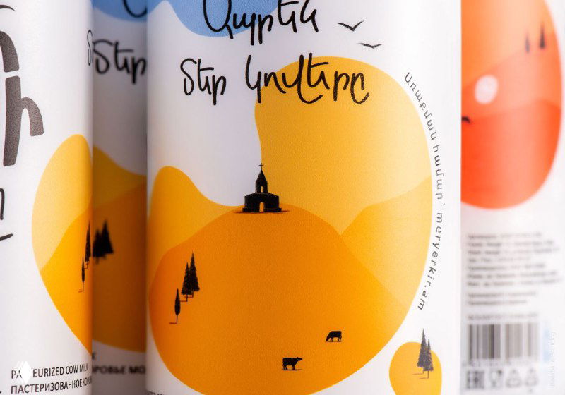 Крупный план этикетки с иллюстрацией пейзажа: горы, домик и силуэты животных в тёплой жёлтой палитре, декоративная типографика.