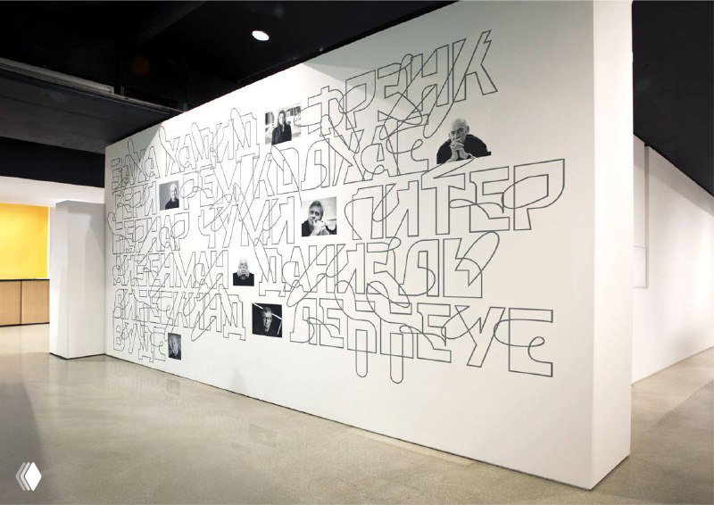 Интерьер галереи с крупной графикой на стене и встраиваемыми экспонатами, интеграция фотографий и типографического рисунка в пространство