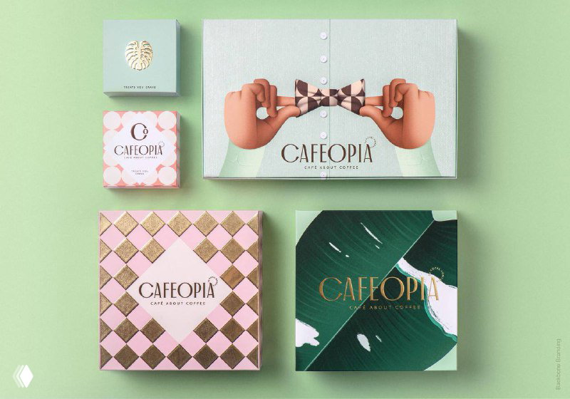 Подарочные коробки Cafeopia с мятно‑розовой палитрой и золотыми деталями; центральная коробка украшена бантом‑иллюстрацией рук в ар‑деко эстетике.