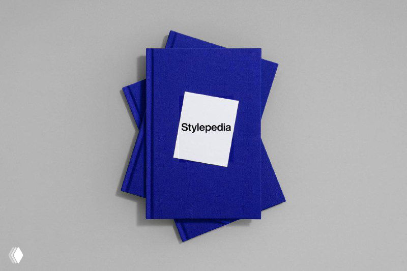 Вид сверху на две перекрывающиеся копии «Stylepedia» с синими текстильными обложками и белым квадратом на лицевой части макета.