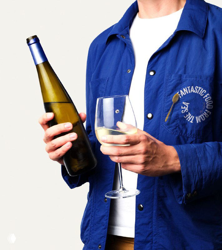 Крупный портрет человека в синей куртке, держащего бутылку и бокал вина; кадр акцентирует брендовую одежду и атмосферу подачи продукта в айдентике Olala.