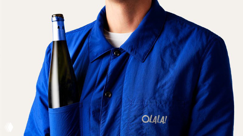 Крупный кадр на синюю куртку с вышитым логотипом Olala и частично видимой бутылкой вина; демонстрация брендированной одежды и упаковочного решения.