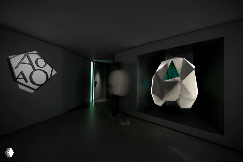 Экспозиция AOAO: объёмная белая скульптура в нише и светящийся контурный логотип на стене в строгом минималистичном пространстве.