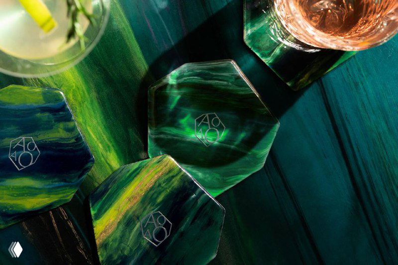 Набор подставок и элементов сервировки из зелёной смолы с тиснением логотипа AOAO, показывающий материалы и текстуры бренда в крупном плане.