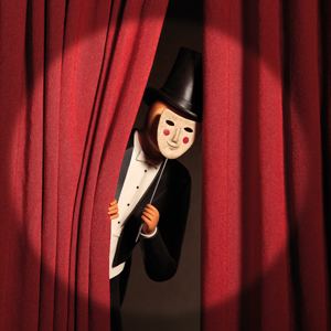 Керамический персонаж в цилиндре выглядывает из-за сцены с красным театральным занавесом: драматическая композиция и тонкая работа с формой и светом
