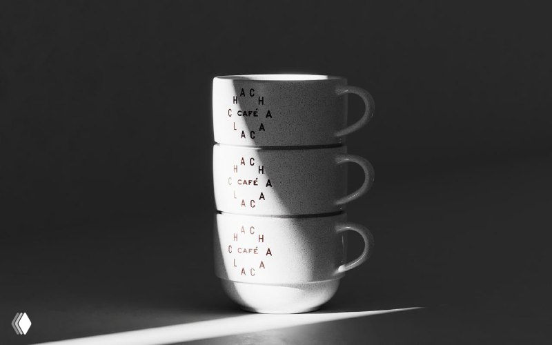 Стопка белых чашек с тонкой типографикой бренда Chachalaca на тёмном фоне — пример минималистичных материалов для сервировки