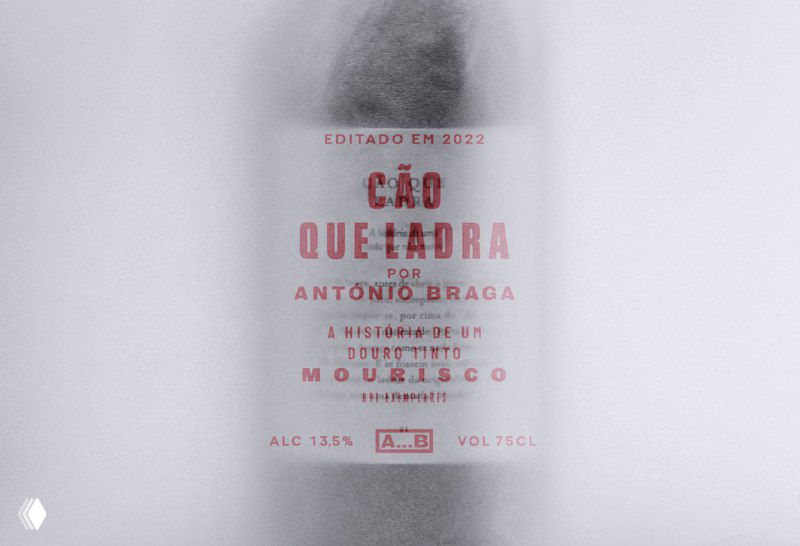 Полупрозрачная шёлковая обёртка крупным планом: виден красный текст названия CÃO QUE LADRA и мелкая типографика на фоне бумаги.