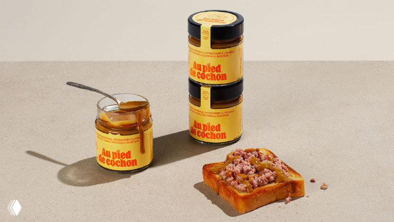 Несколько банок и тюбиков продукта разных размеров, выстроенные на столе: единая цветовая палитра и яркие оранжевые надписи на этикетках.