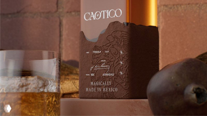 Крупный план нижней части бутылки Caotico с тёмно-коричневой рельефной этикеткой, на фоне бокала с напитком и кусков фруктов.