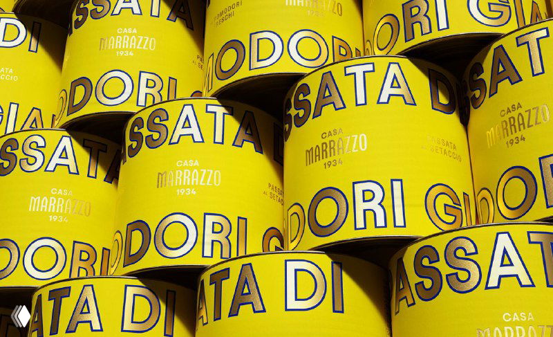 Ряд жёлтых банок Casa Marrazzo, образующих графический паттерн с крупной надписью и контрастной окантовкой; изображение подчёркивает повторяемость и узнаваемость дизайна упаковки.