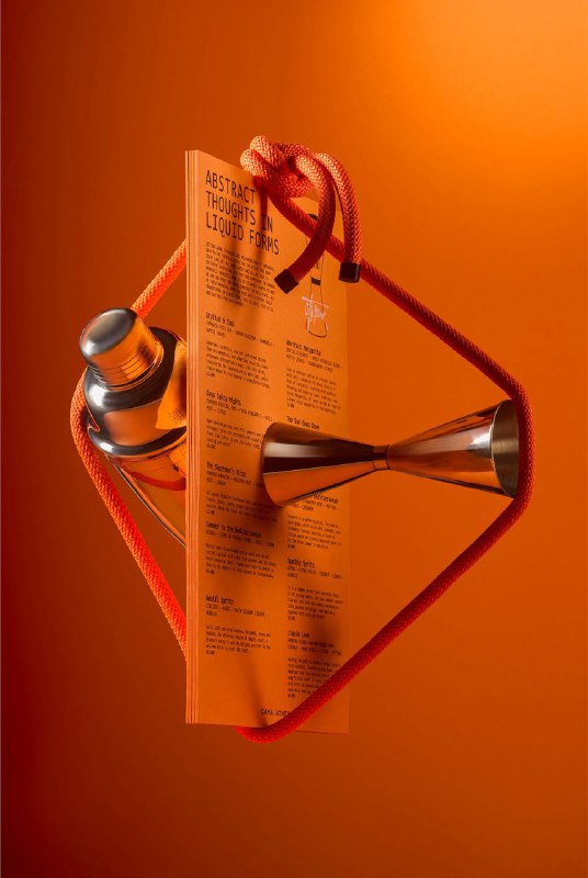 Меню и печатные листы Gaya Athens в динамичной композиции с верёвками и металлическим предметом на оранжевом фоне; кадр подчёркивает объём и конструкцию презентации.