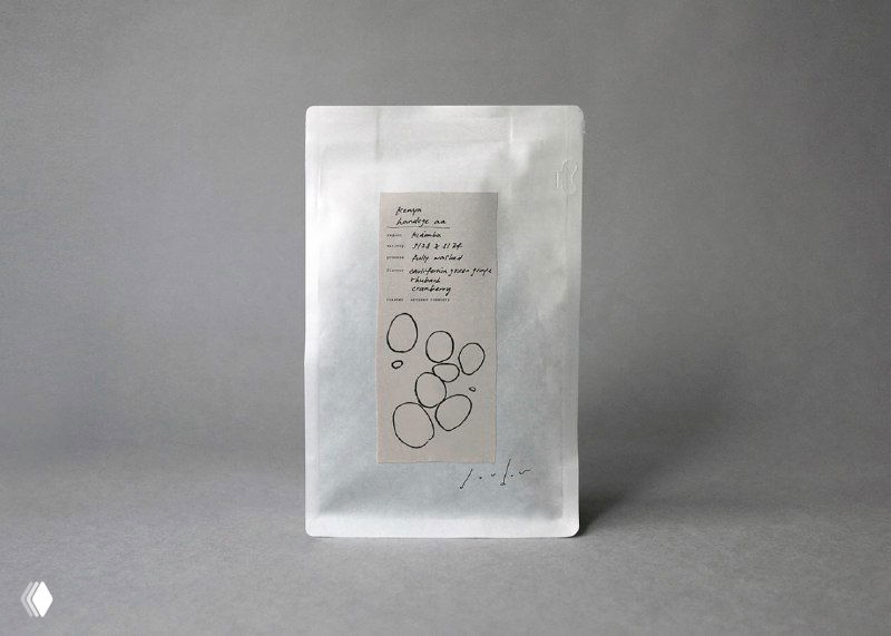 Фотография белого пакетика для кофе с этикеткой проекта Dou dou: сдержанная бумажная текстура и рукописная графика кругов на стикере в центре.