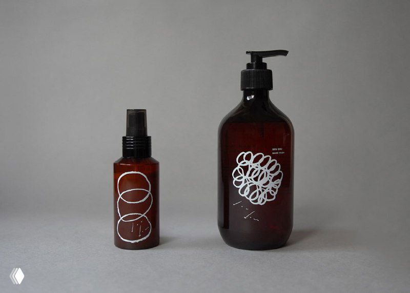 Две стеклянные тёмные флакона с дозатором и спреем, украшенные белой рукотворной графикой — пример применения айдентики Dou dou на бутылочной упаковке.